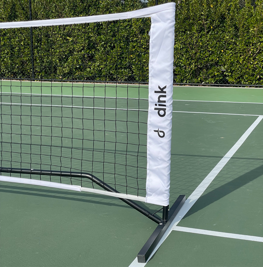 Pickleball net with a white padding strip featuring the 'dink' logo on a green tennis court.