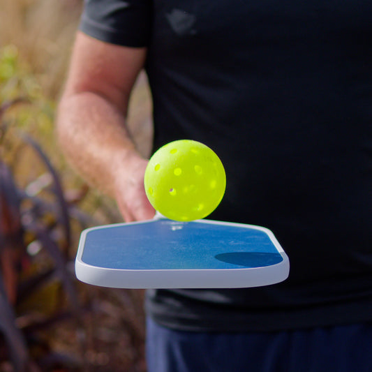 Person holding a paddle with a yellow ball on top outdoors